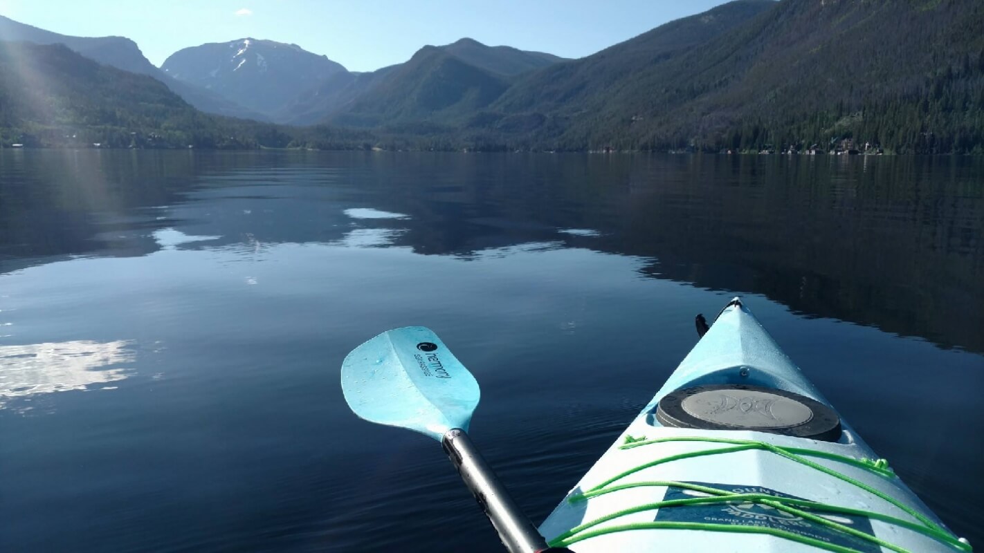 A serene lake scene with a kayak paddle resting on the water's surface, surrounded by mountains and trees in Grand County Colorado.