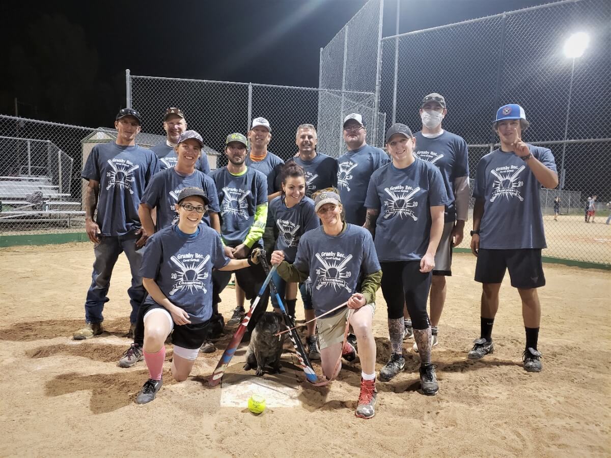 A group of smiling softball players pose together on a sandy field at night in Grand County Colorado.