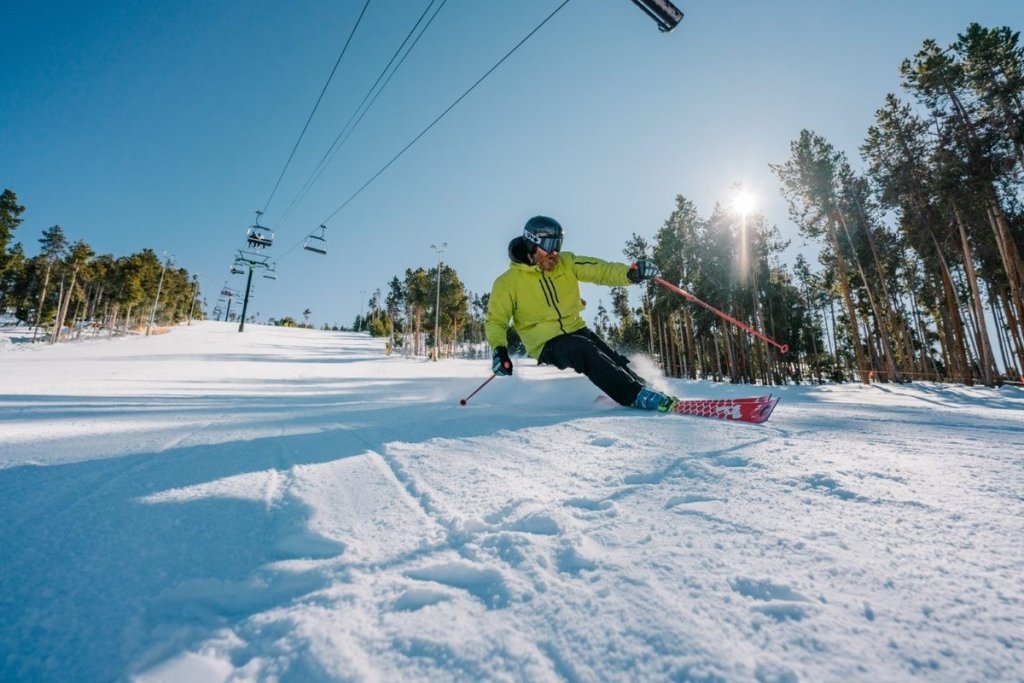 A skier in a yellow jacket and black pants carves a turn on a snowy slope in Grand County Colorado.