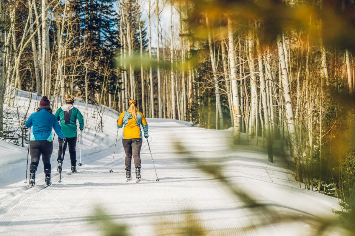 Three skiers glide down a snow-covered trail surrounded by tall trees in Grand County Colorado.