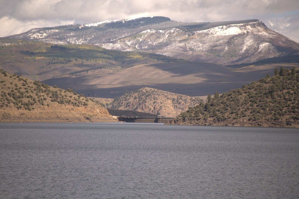A serene lake stretches towards distant snow-capped mountains under a cloudy sky in Grand County Colorado.