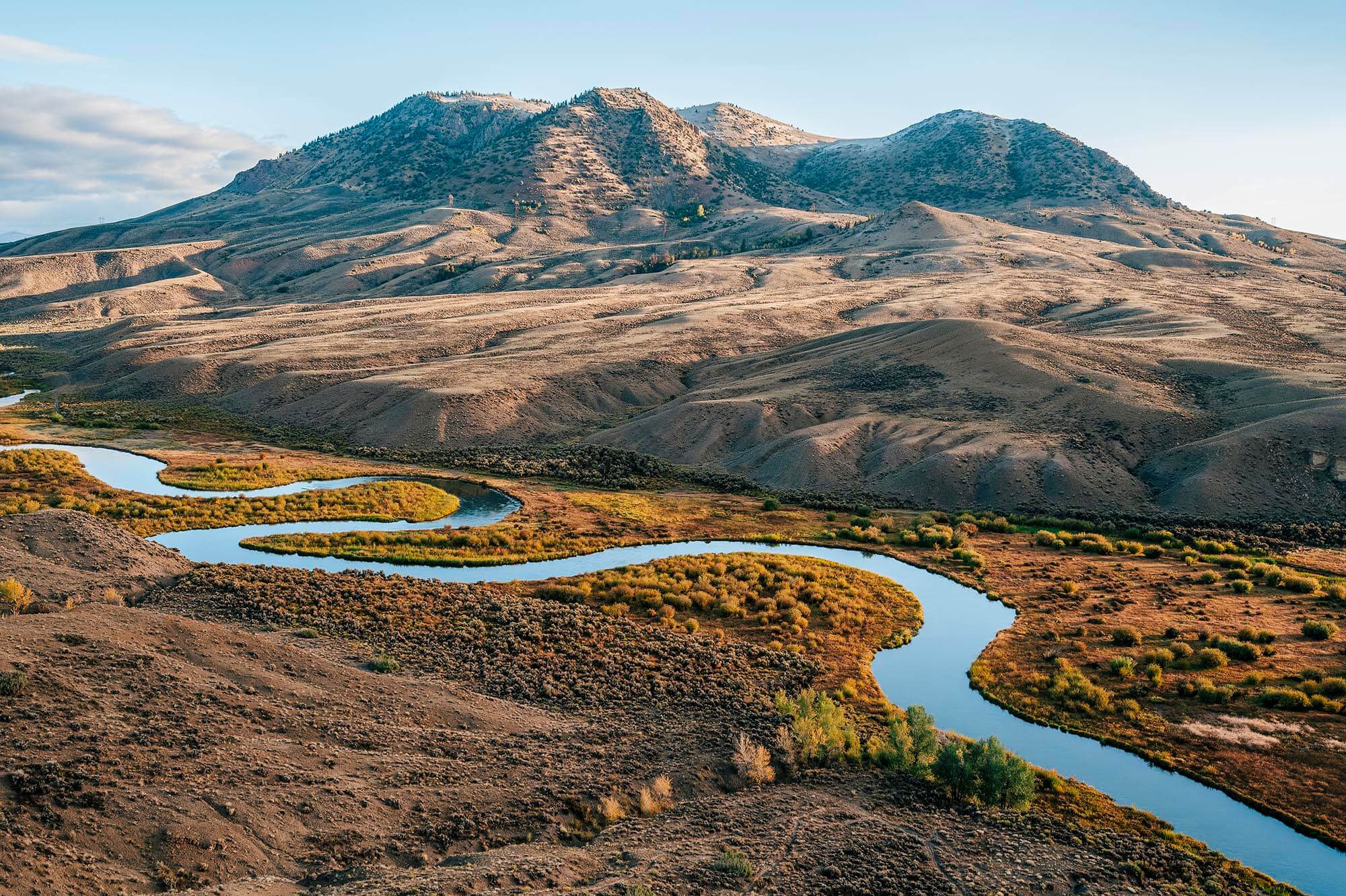 A winding river snakes through a vast, arid landscape with distant mountains in Grand County Colorado.