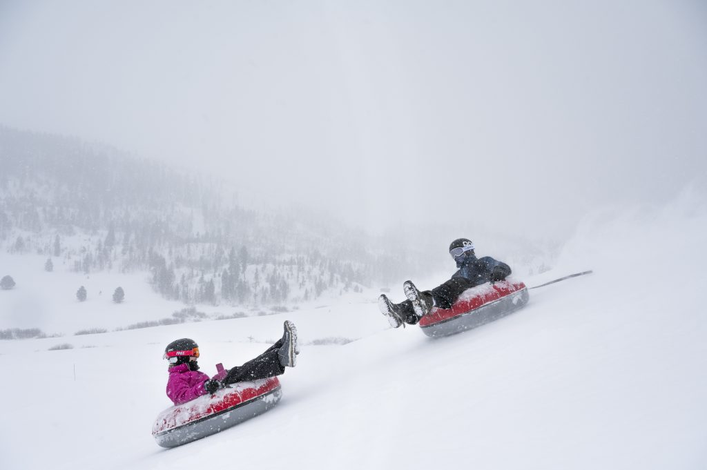 Two people snow tubing down a snowy hill at C Lazy U Ranch on a winter day.