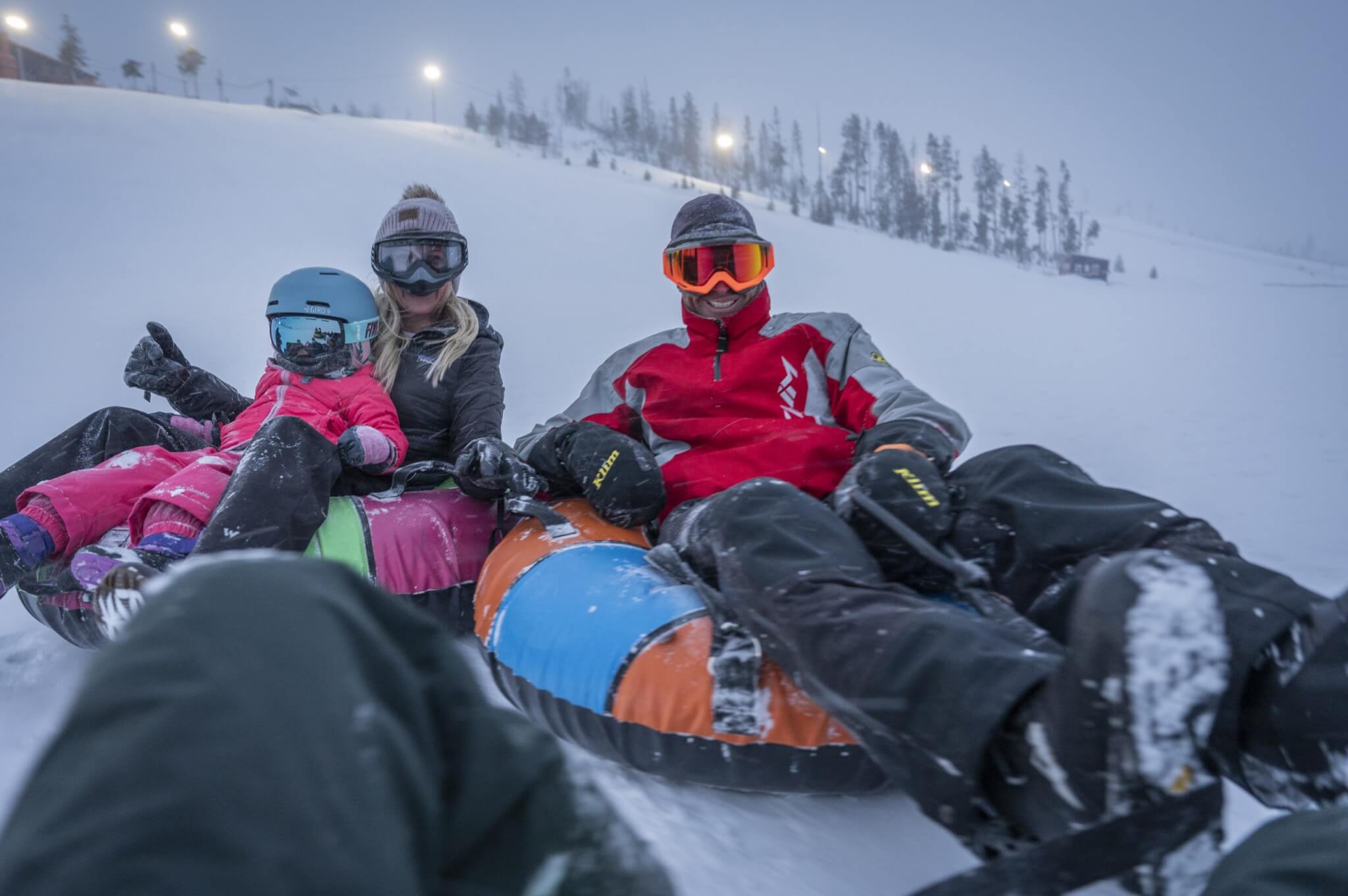 A family enjoys a snowy day, tubing down a hill with colorful inflatable tubes in Grand County Colorado.