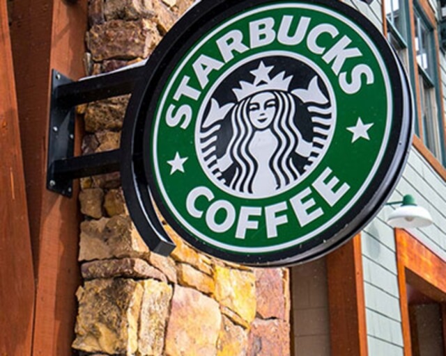 A green Starbucks Coffee sign with the iconic mermaid logo is mounted on a stone wall in Grand County Colorado.