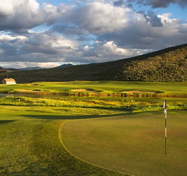 A serene golf course with rolling hills, a pond, and a distant house under a cloudy sky in Grand County Colorado.