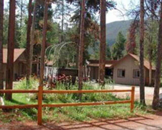 A serene forest scene with a wooden fence, tall trees, and rustic cabins in Grand County Colorado.