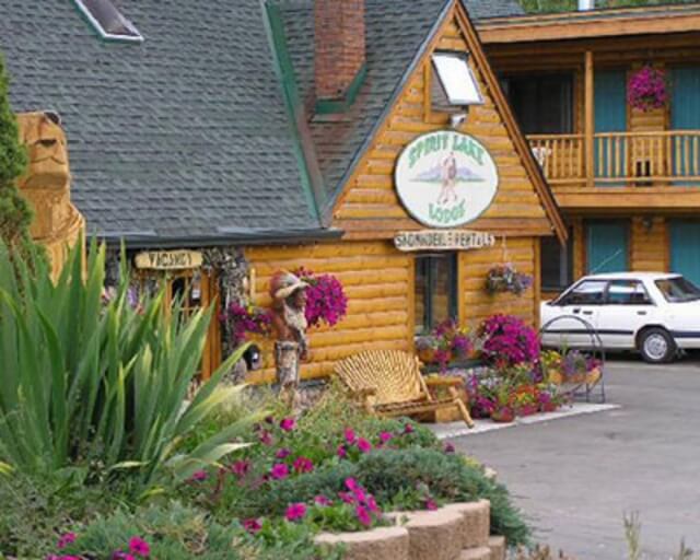 A charming wooden lodge with a rustic sign, surrounded by vibrant flowers and greenery in Grand County Colorado.