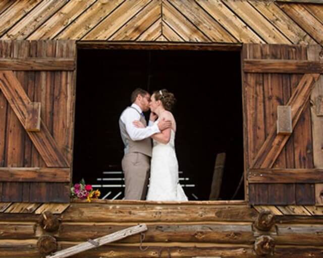 A bride and groom share a kiss in the doorway of a rustic wooden barn in Grand County Colorado.