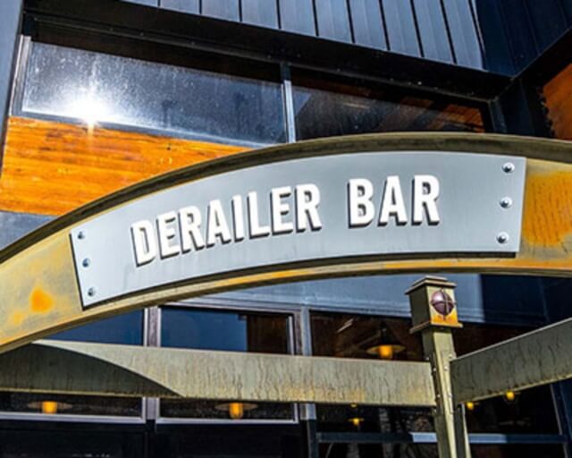 A metal archway with the words 'Derailer Bar' in white letters above a building entrance in Grand County Colorado.