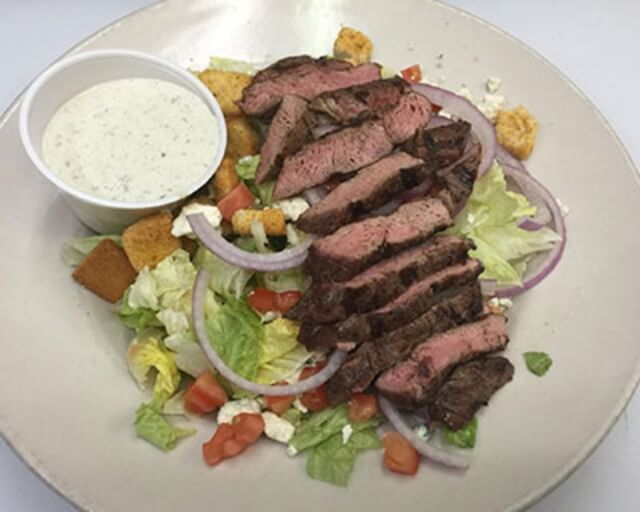 A plate of steak salad with lettuce, tomatoes, onions, croutons, and a side of dressing in Grand County Colorado.