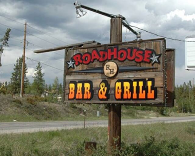 A weathered wooden sign for Roadhouse Bar & Grill stands by the roadside in Grand County Colorado.
