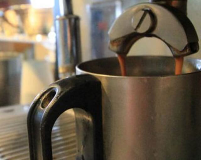 A stainless steel pitcher with a black handle is being filled with espresso from a machine in Grand County Colorado.