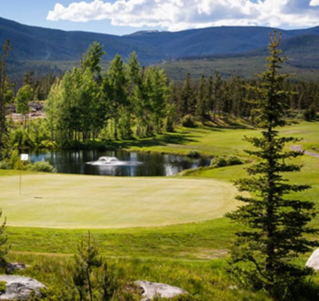 A serene golf course with a pond, fountain, and surrounding mountains in Grand County Colorado.