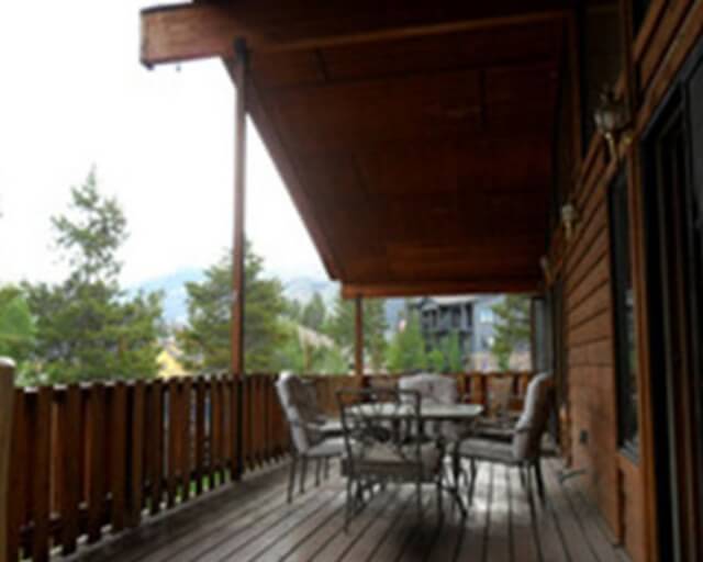 A wooden deck with a table and chairs overlooks a forested area and distant mountains in Grand County Colorado.