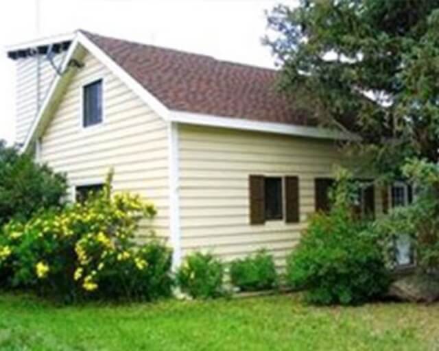 A quaint, yellow house with a brown roof nestled among lush greenery and yellow flowers in Grand County Colorado.