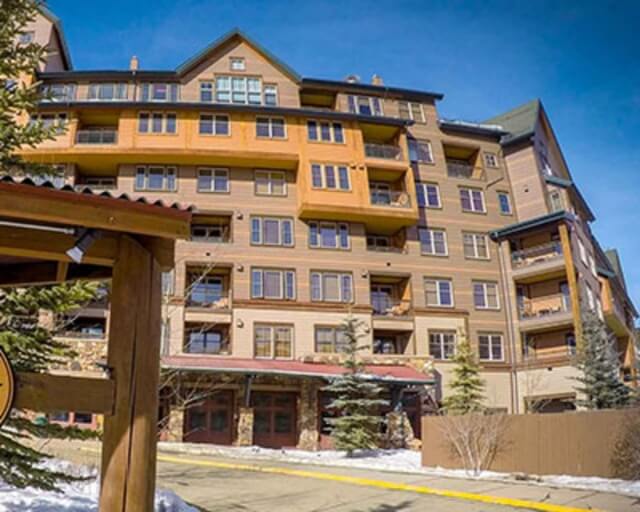 A multi-story mountain resort building with balconies and a stone base, surrounded by snow and trees in Grand County Colorado.