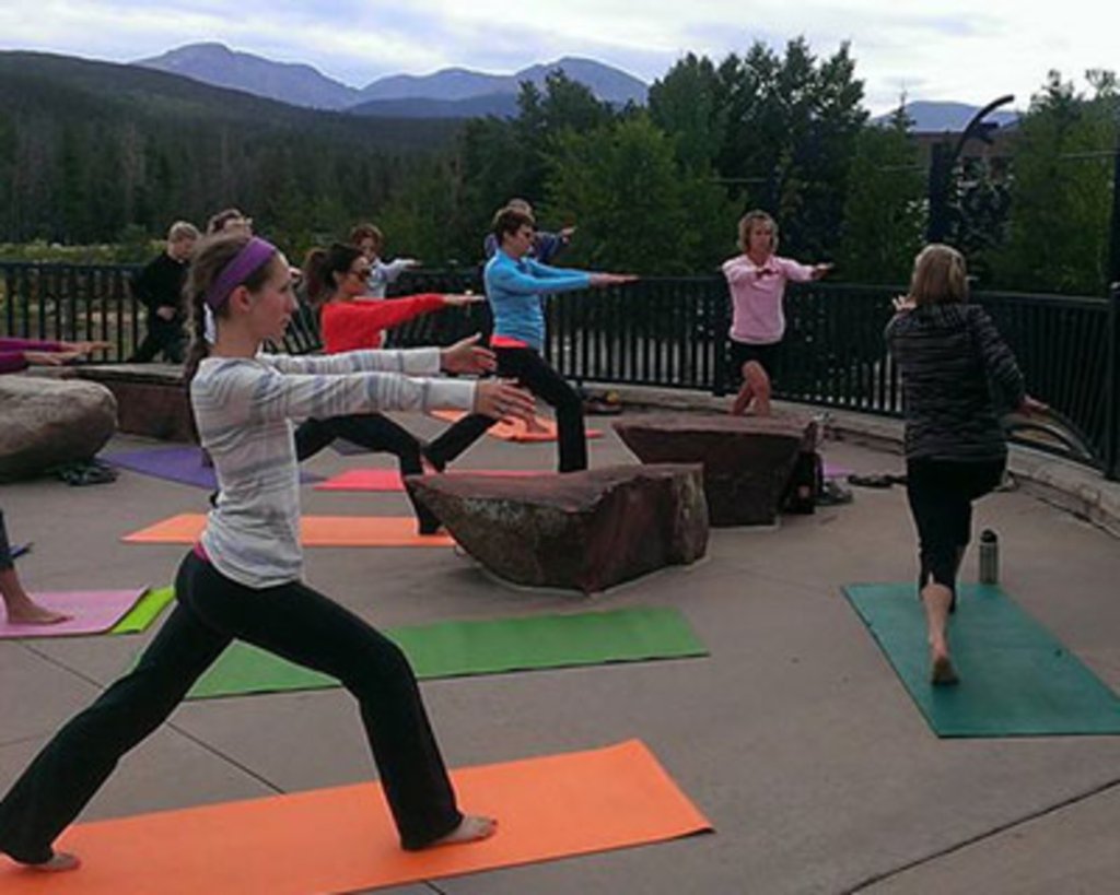 A group of people practicing yoga on colorful mats outdoors with mountains in the background in Grand County Colorado.
