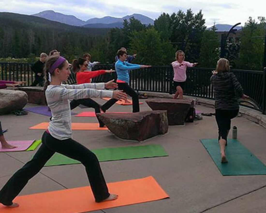 A group of people practicing yoga on colorful mats outdoors with mountains in the background in Grand County Colorado.