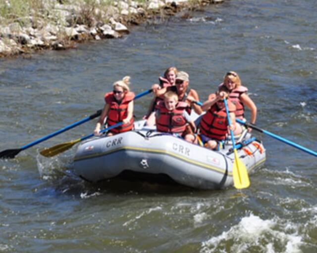 A group of people in a raft navigate rapids on a river, wearing life jackets and using oars in Grand County Colorado.
