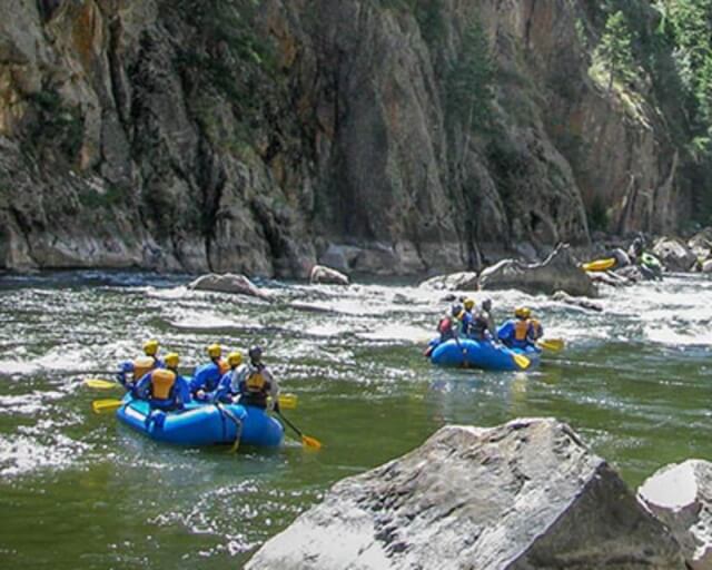 Two rafts of people in life jackets navigate white water rapids near rocky cliffs in Grand County Colorado.