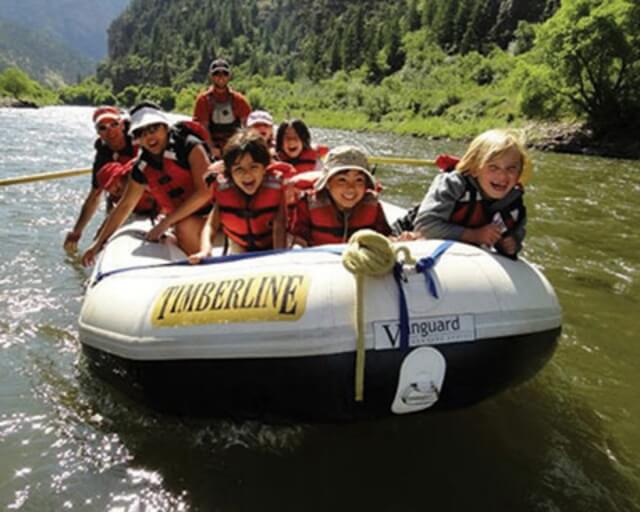 A group of smiling people in life jackets raft down a river in Grand County Colorado.