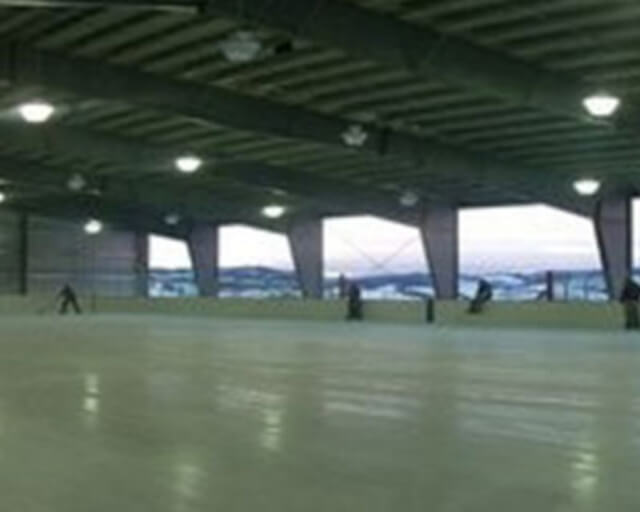 A large indoor ice rink with several people skating and a view of the outdoors through large windows in Grand County Colorado.