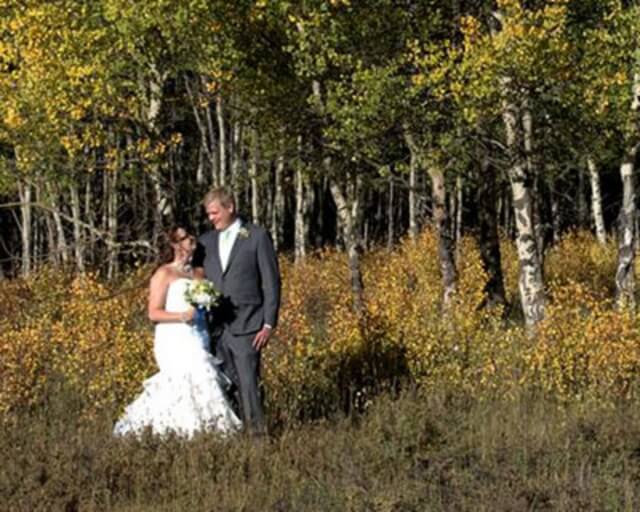 A bride and groom stand amidst a vibrant autumn forest, surrounded by golden leaves in Grand County Colorado.