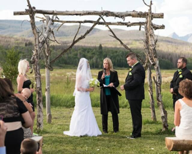 A rustic outdoor wedding ceremony with a wooden arch and a bride and groom exchanging vows in Grand County Colorado.
