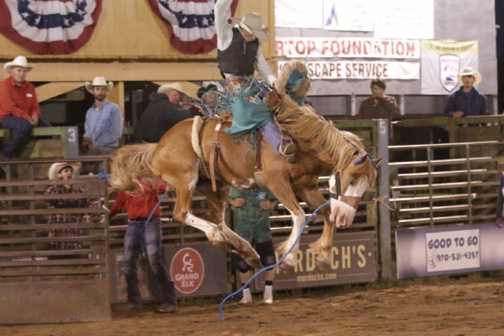 Cowboy riding bucking bronco at rodeo, waving American flag in victory in Grand County Colorado.