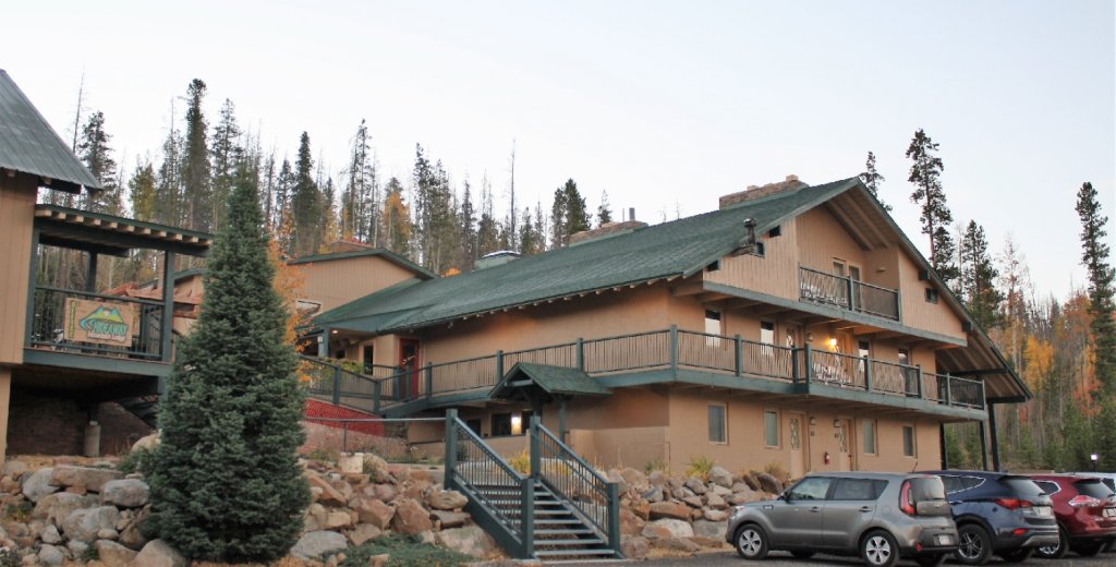A rustic, multi-story lodge with balconies and a staircase, nestled among tall trees in Grand County Colorado.