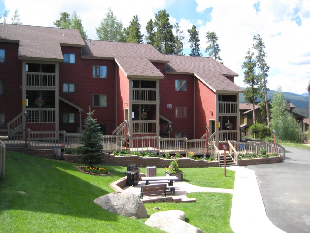 A red apartment building with balconies and a landscaped courtyard featuring a picnic table and benches in Grand County Colorado.