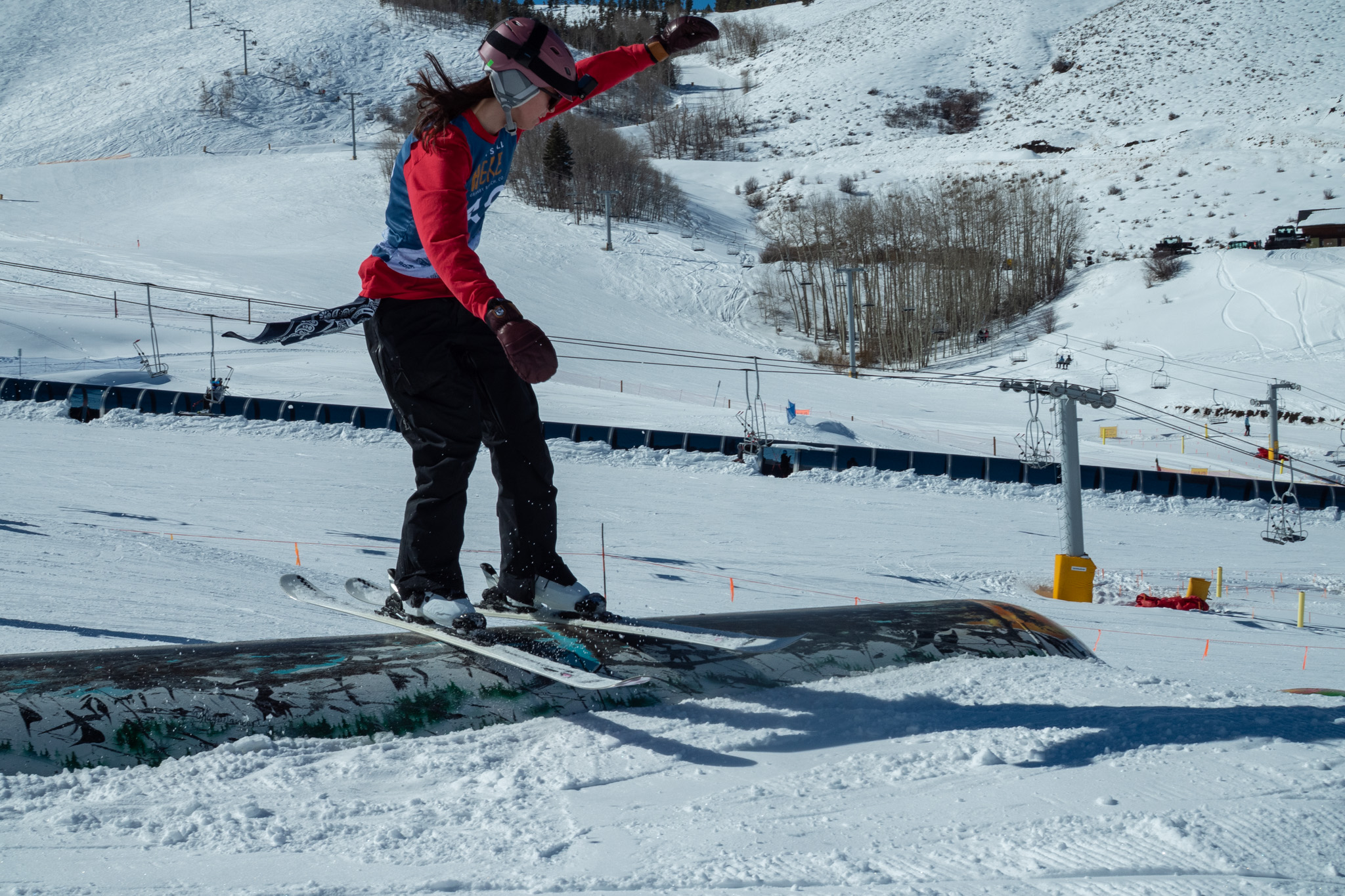 A snowboarder in a red jacket grinds on a rail in a snowy terrain park in Grand County Colorado.