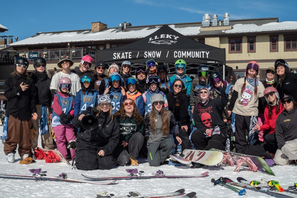 A large group of skiers and snowboarders pose together in front of a tent at a snowy mountain resort in Grand County Colorado.