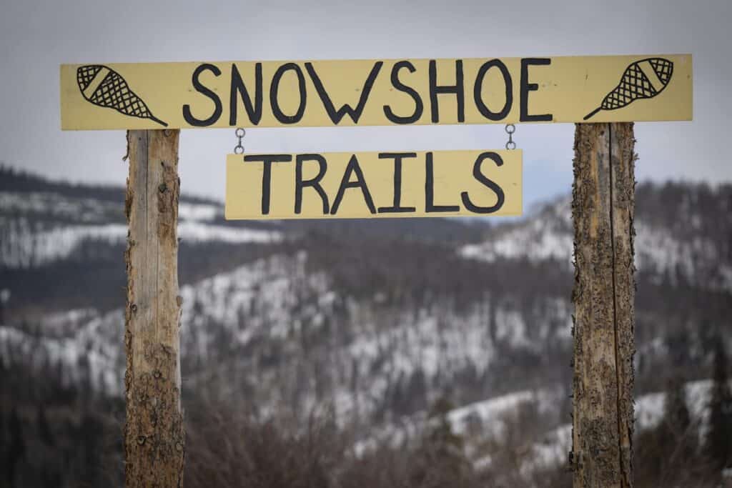 A sign that says "snowshoe trails" with the Rocky Mountains in the background