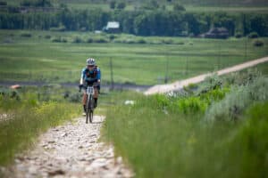 Cyclist with the number 73 competes in an off-road race on a rocky path through a grassy landscape.