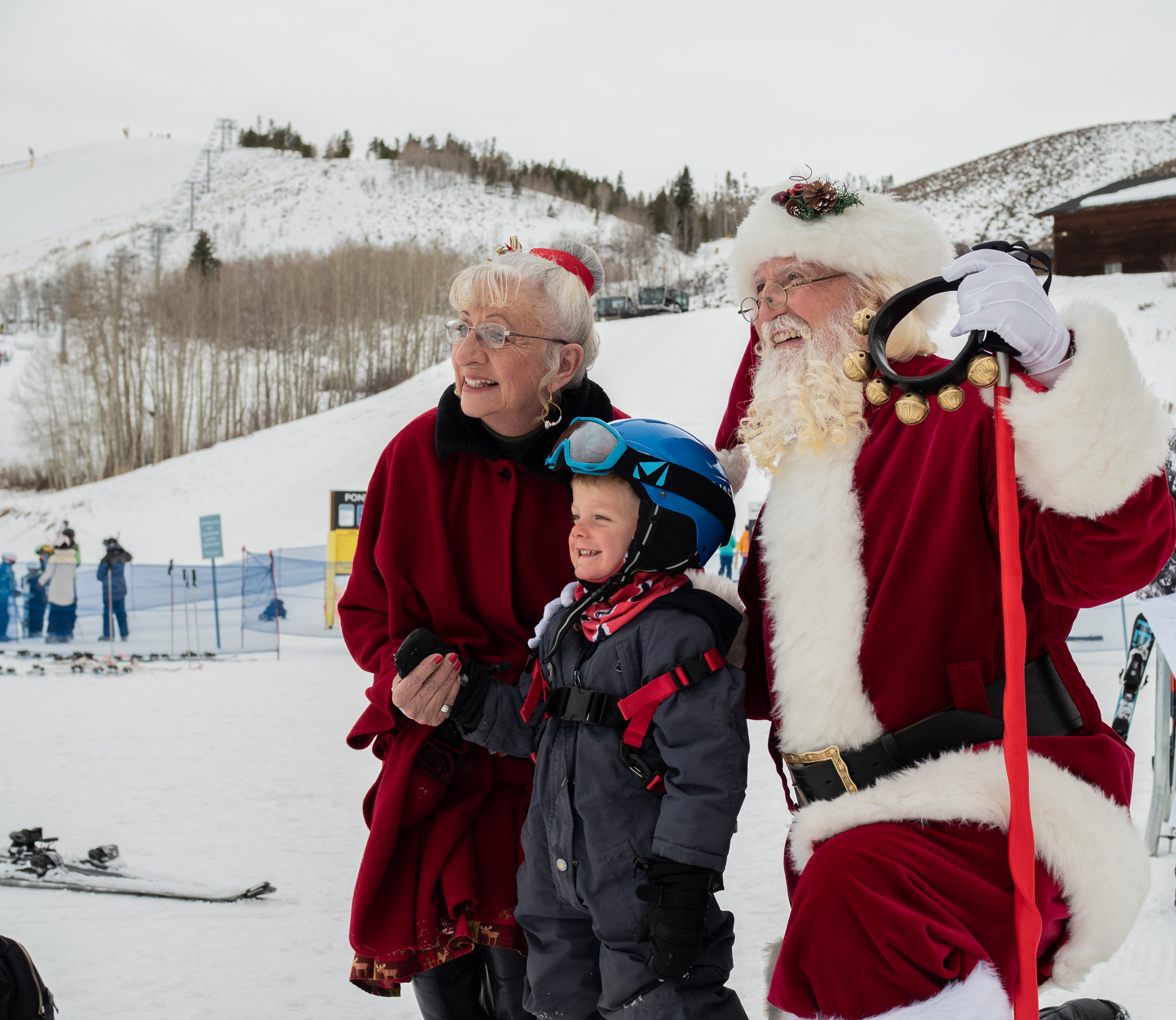 A family dressed in festive attire poses with Santa Claus on a snowy ski slope in Grand County Colorado.