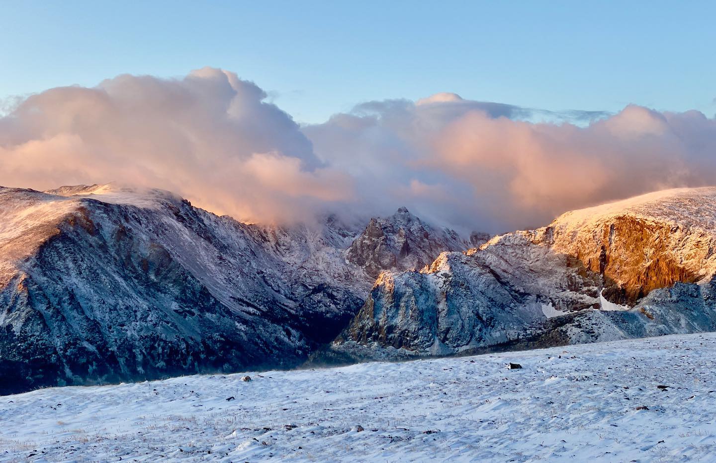 A snow covered mountain range with clouds in the sky.