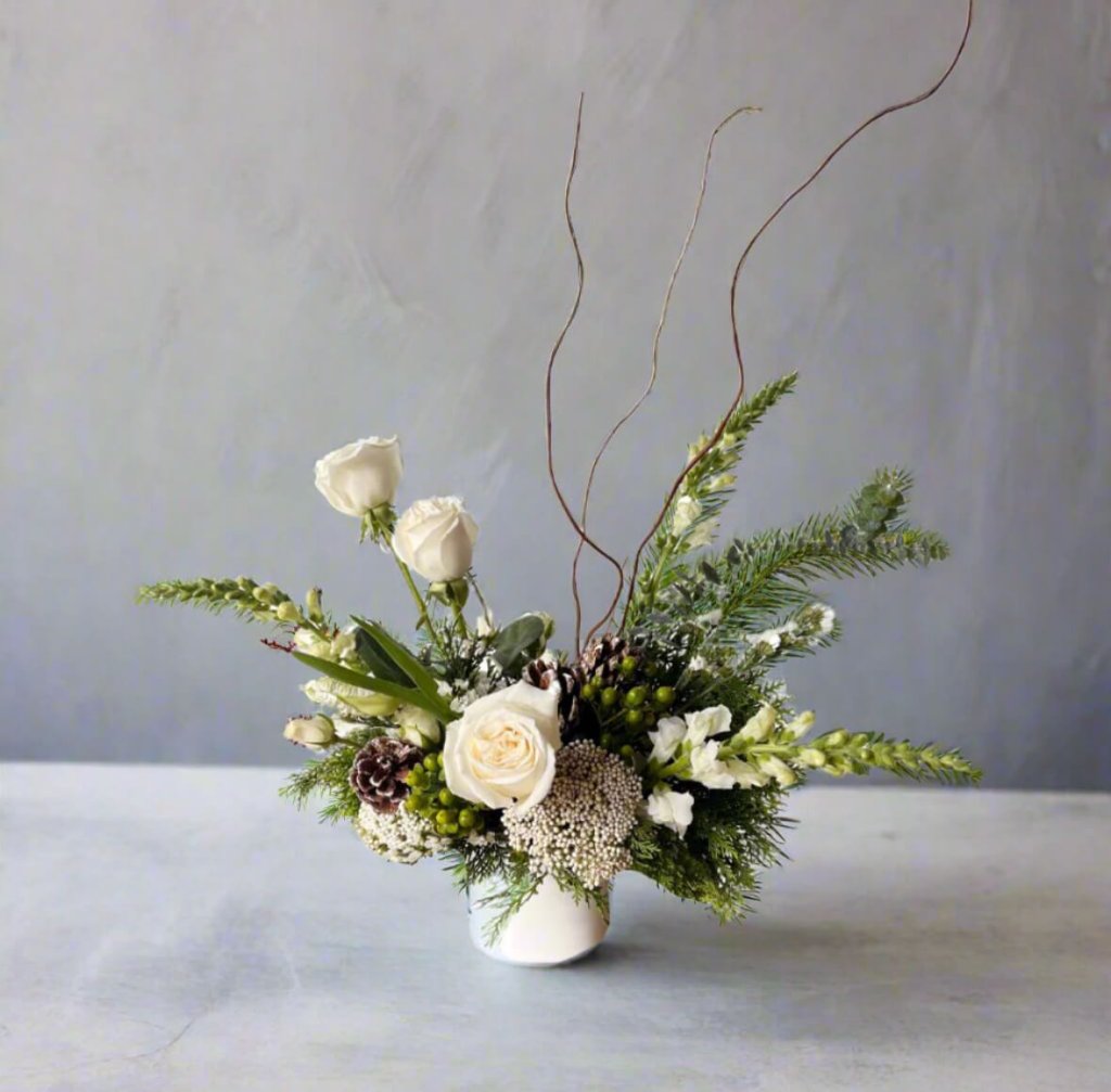 A delicate white rose bouquet with pinecones and greenery in a white vase in Grand County Colorado.