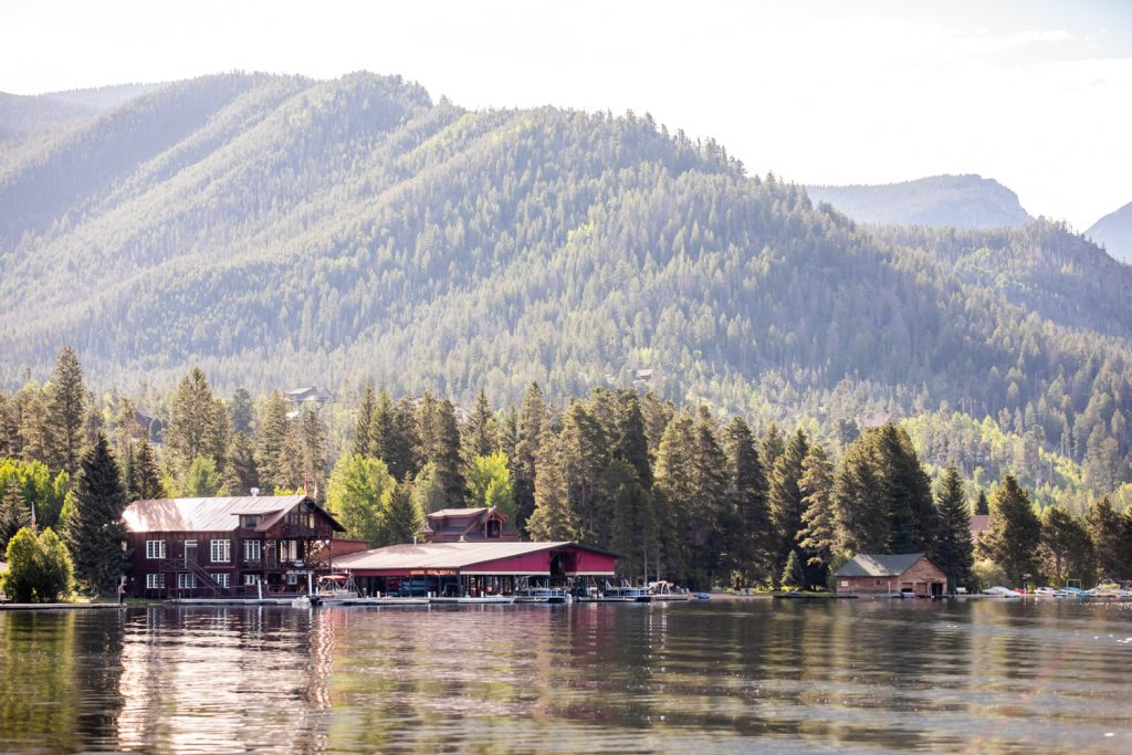 Grand Lake Marina with rustic lakeside buildings, calm water, and forested mountains in the background.