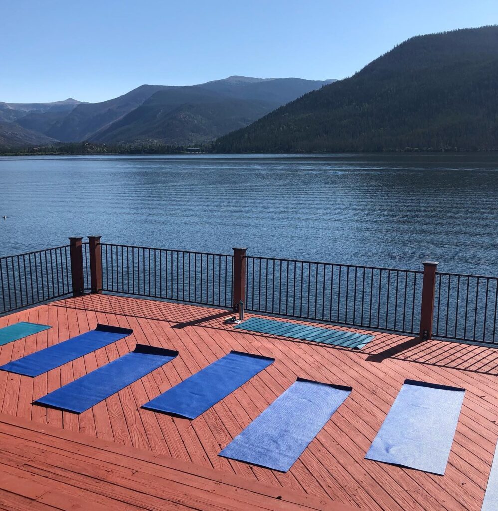 Four yoga mats on a deck overlooking a lake.