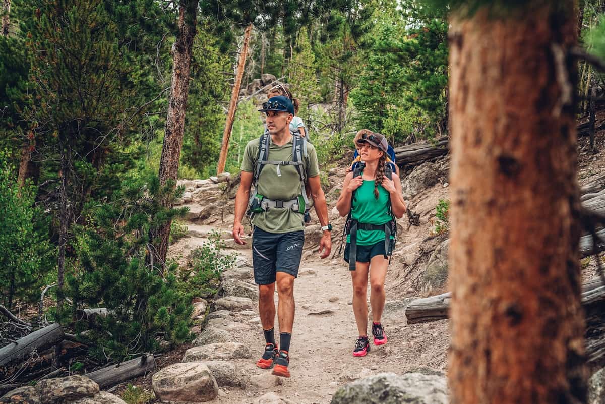Three hikers with backpacks walk along a rocky mountain trail surrounded by trees in Grand County Colorado.