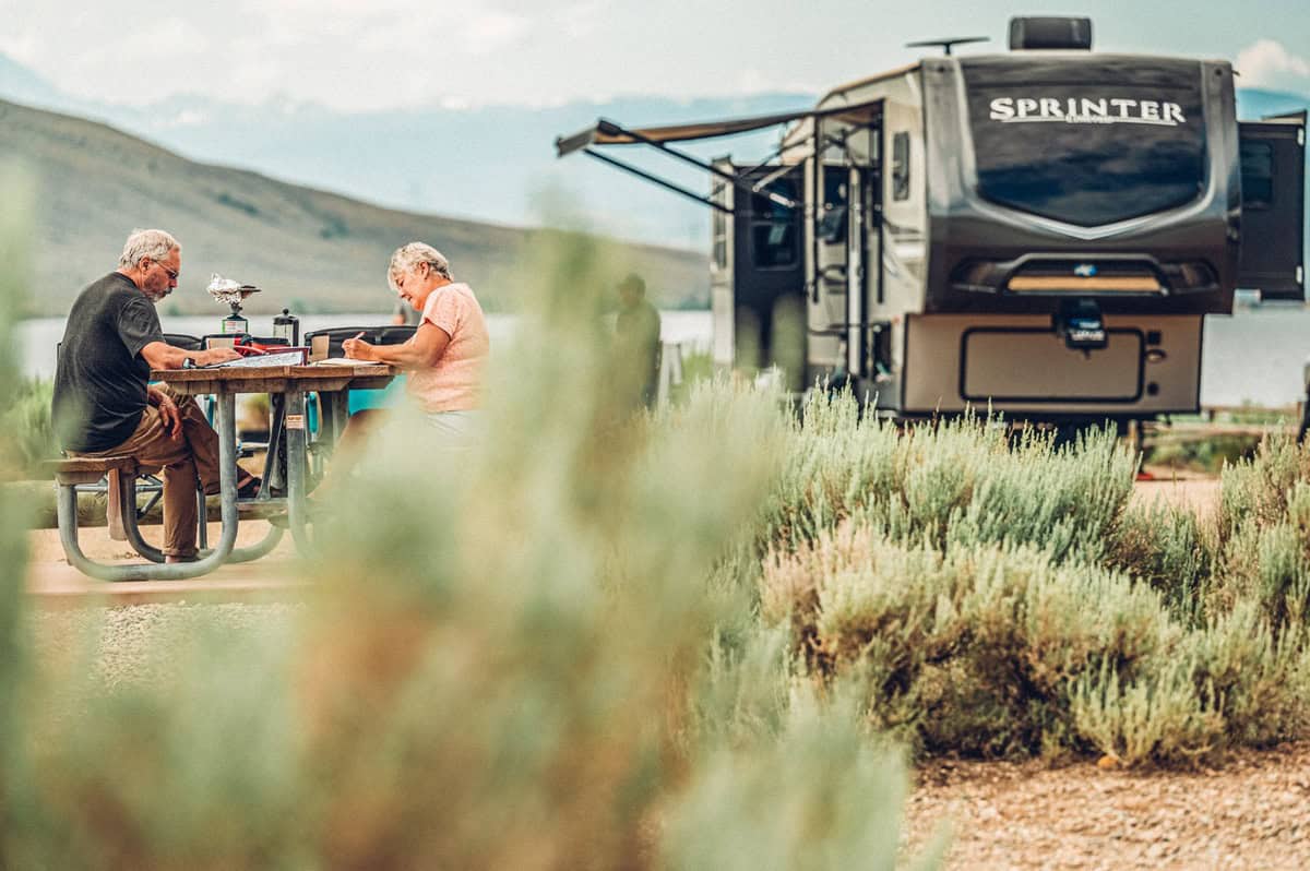 A family sits at a picnic table by an RV parked at a Lake Granby campground
