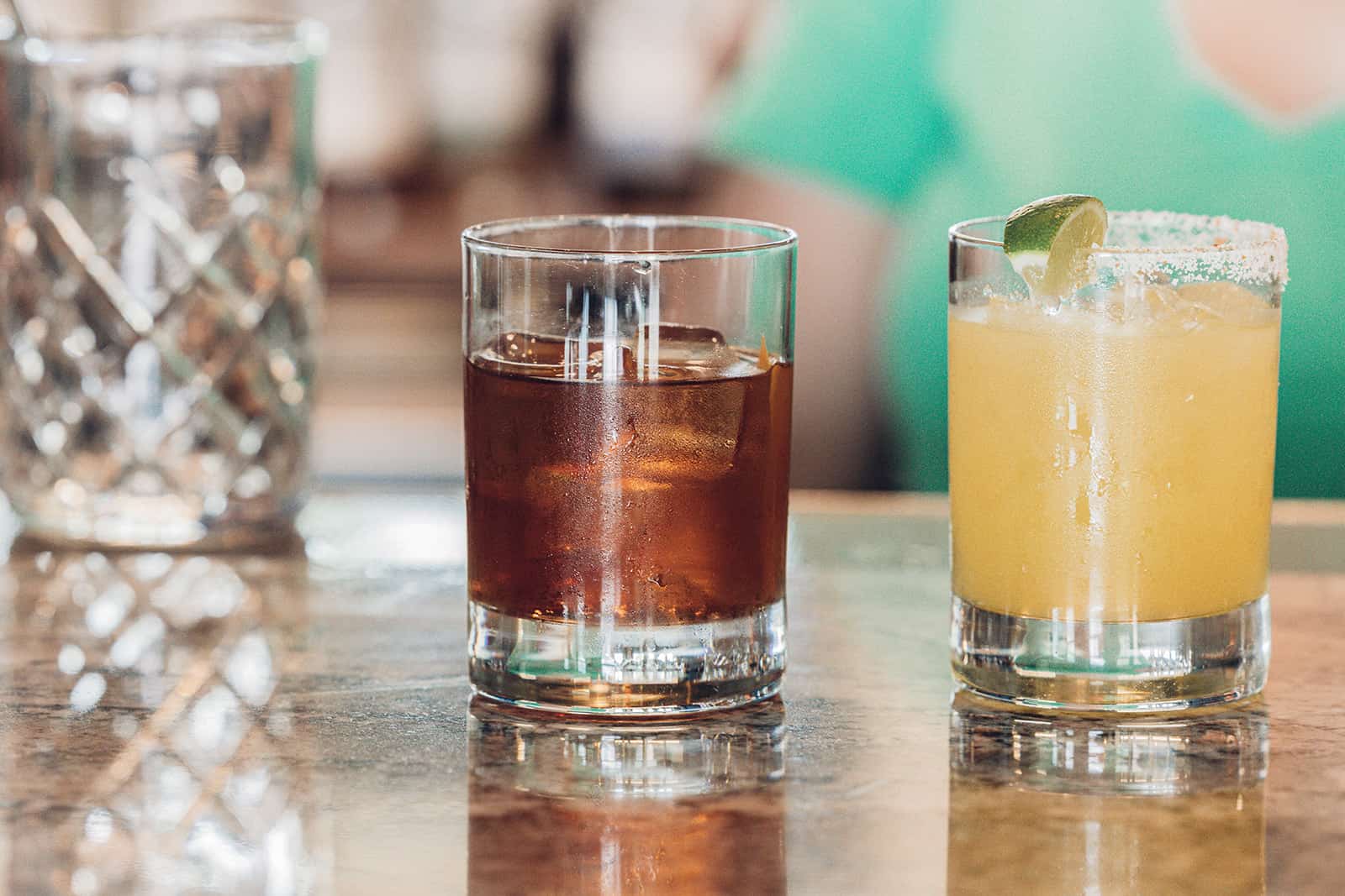 A woman is sitting at a bar with a drink in front of her.