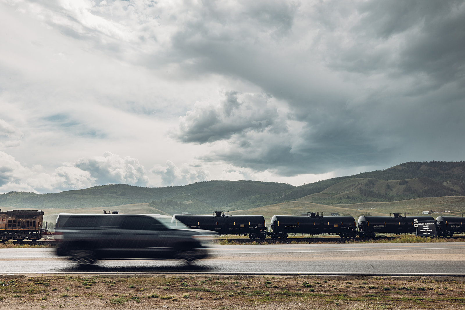 A dark SUV speeds past a long train of black tanker cars on a highway in Grand County Colorado.