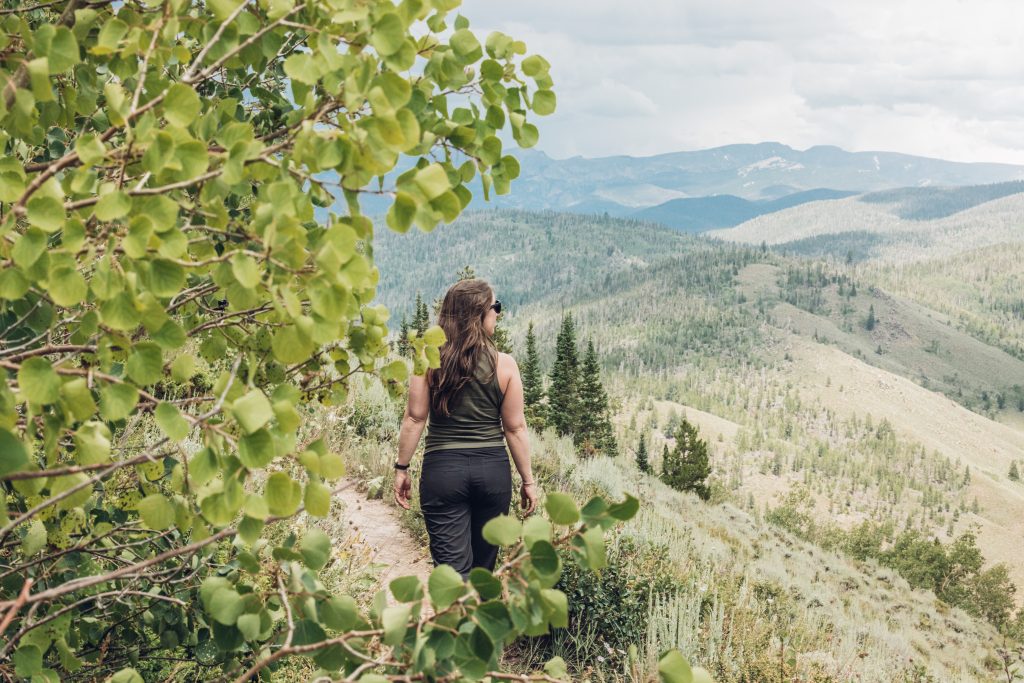 Person hiking a trail at Granby Ranch, surrounded by green trees and overlooking rolling forested mountains.