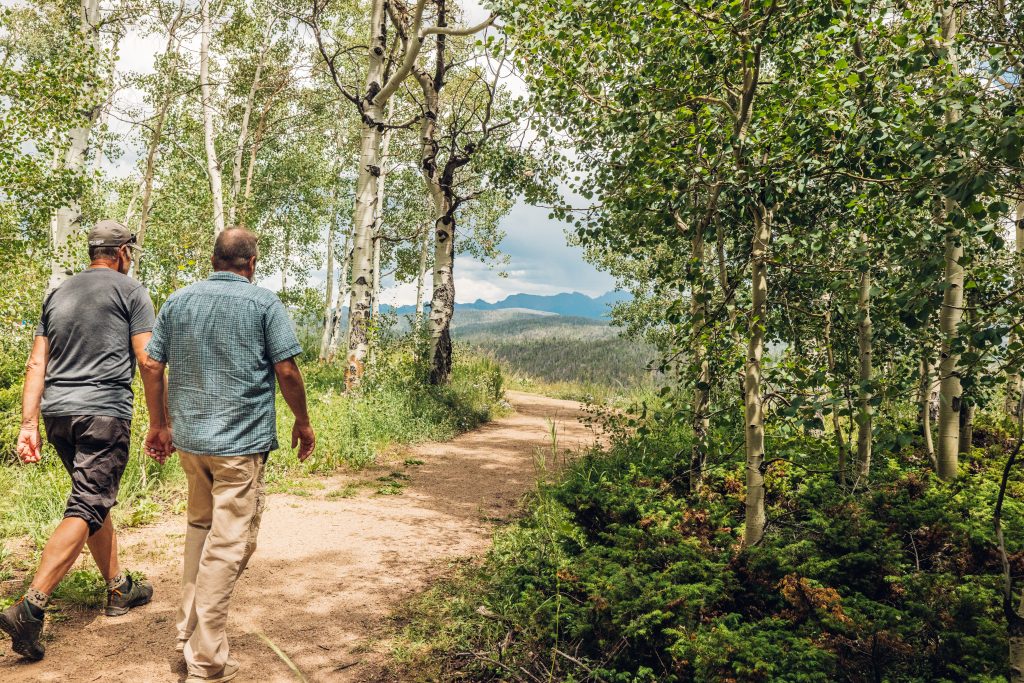 Two men walking on a forest trail at Granby Ranch with mountain views.