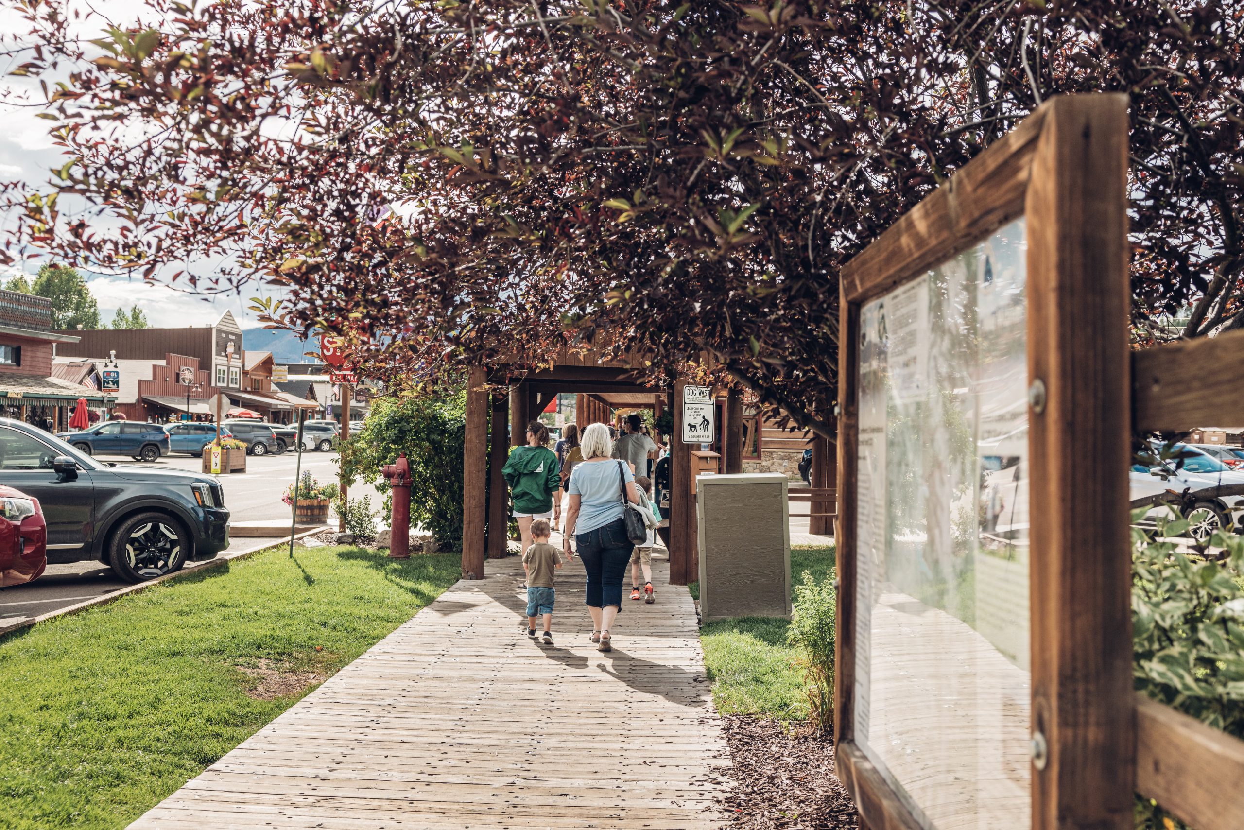 A family walks down a wooden boardwalk lined with trees and shops in Grand County Colorado.