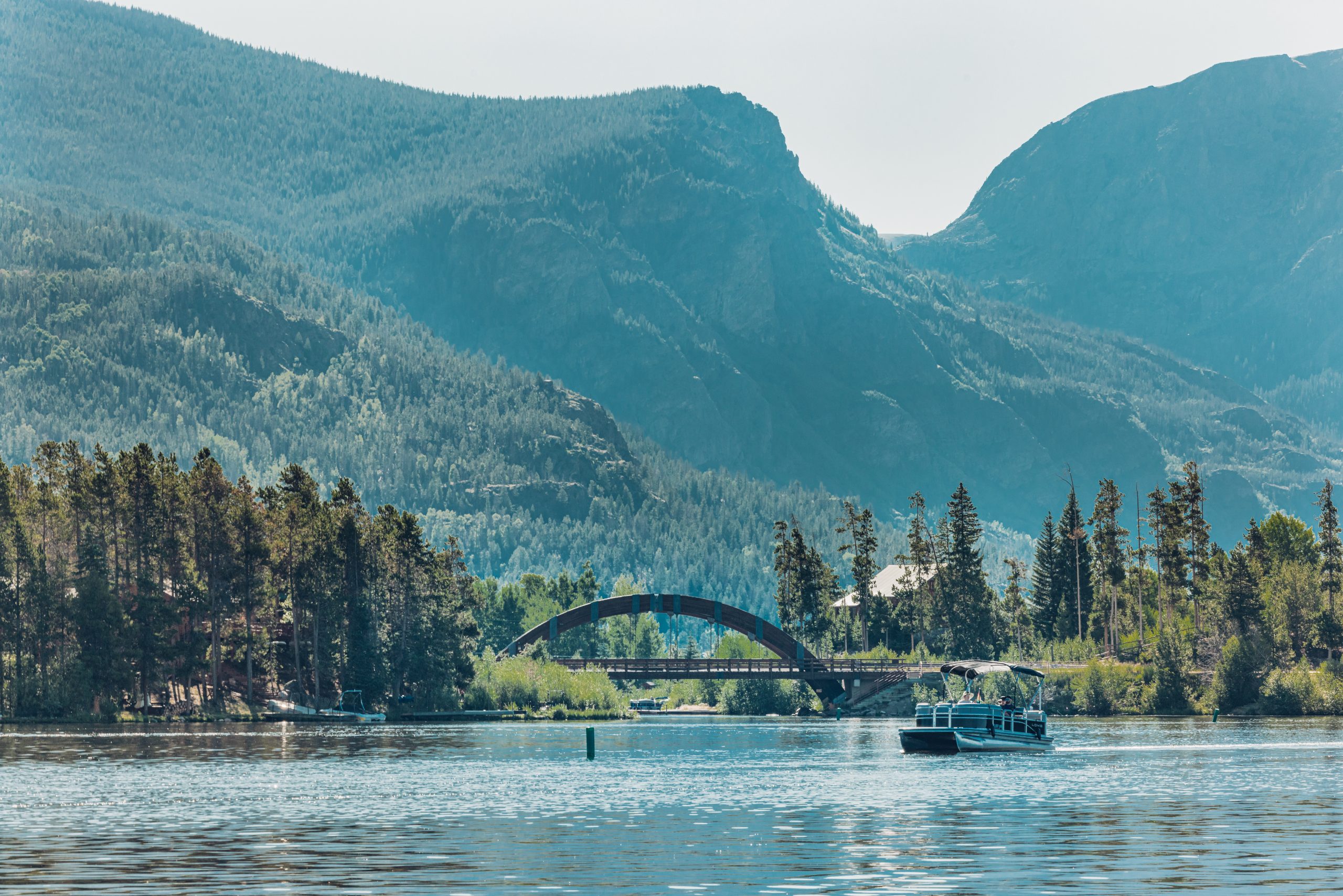 A serene lake with a boat, framed by a forested shoreline and a mountain backdrop in Grand County Colorado.