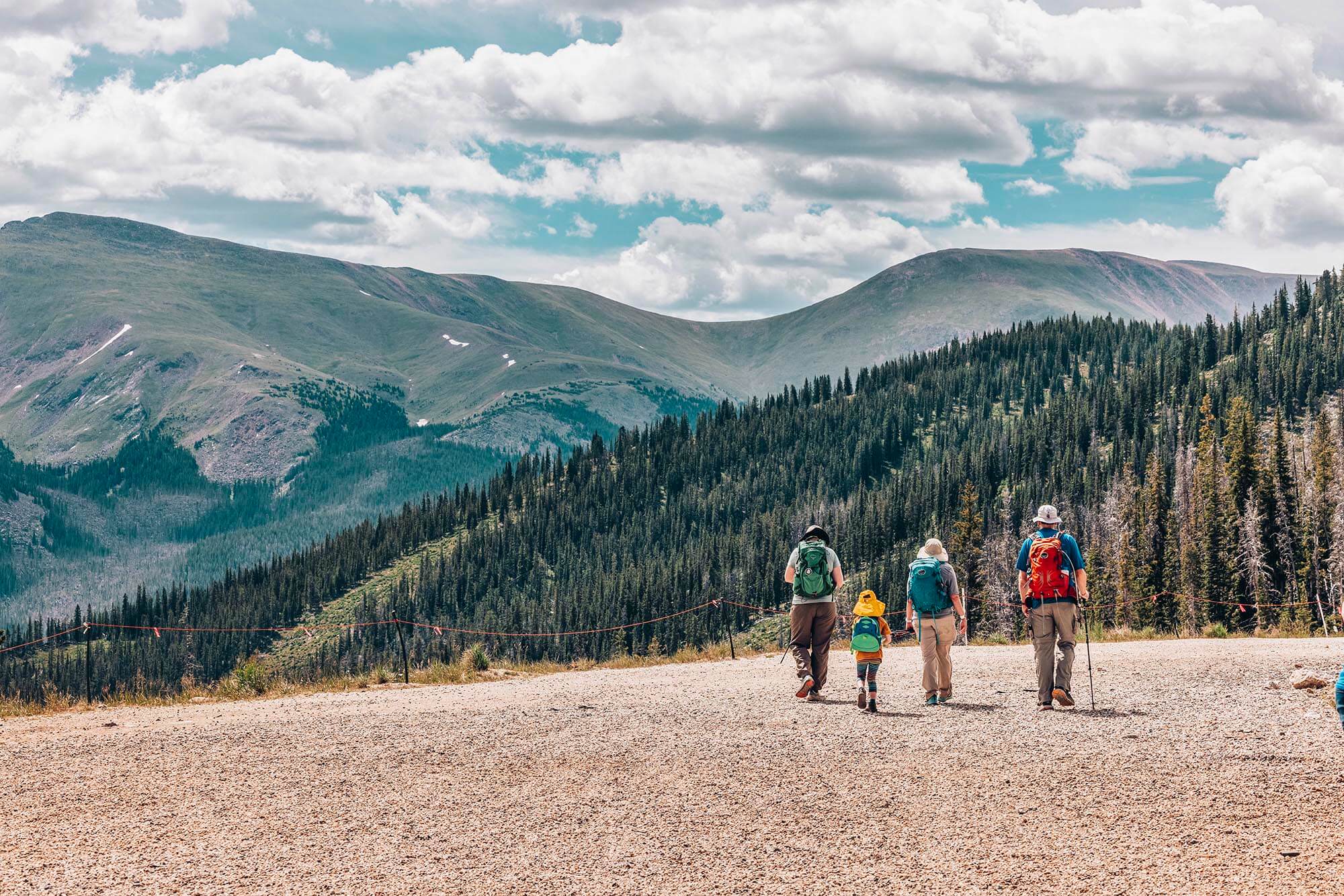 A family of four, including two children, hikes along a mountain trail with backpacks in Grand County Colorado.